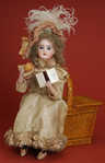A Lambert Child seated on picnic basket automaton, having a Jumeau head and a brass musical clockwork mechanism concealed in the basket