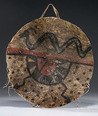 A Pueblo polychrome-painted hide shield, detailed with an Avanyu on top half and an abstract design with lightning bolts and dots on lower half; painted in red, green, yellow, and black; with hide thongs looped through edges