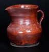 A glazed redware pitcher, attributed to Henry Schofield, Cecil County, Maryland, circa 1930, squat-form pitcher with footed base and coggled geometric designs